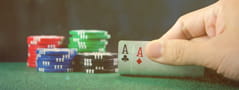 Cuatro montones de fichas de casino de distintos colores y una mano levantando un cuarto de dos naipes: un as de trébol y uno de picas.